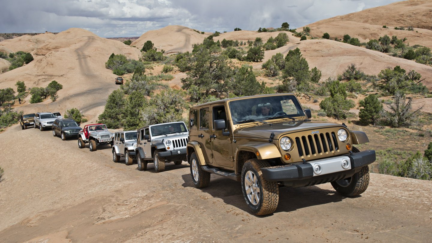 Bronze Jeep Wrangler Unlimited leading a convoy of Wranglers and Grand Cherokees across slickrock among juniper trees near Moab, Utah.